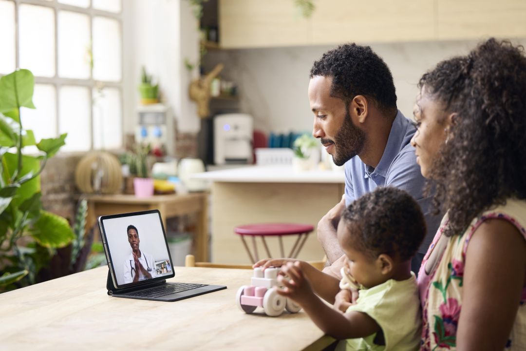 Family of three sitting at a table, talking to a telehealth provider on a tablet